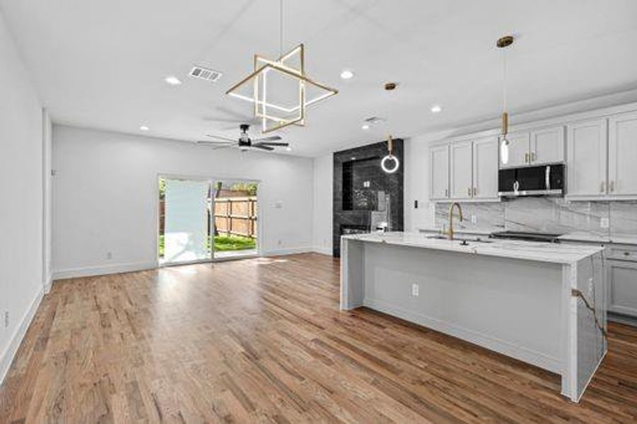 Kitchen with ceiling fan, an island with sink, tasteful backsplash, decorative light fixtures, and light hardwood / wood-style floors