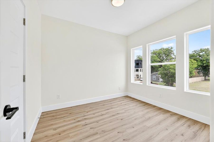 Light-filled room featuring three large windows, neutral-toned walls, wood-finish flooring, and crisp white baseboards