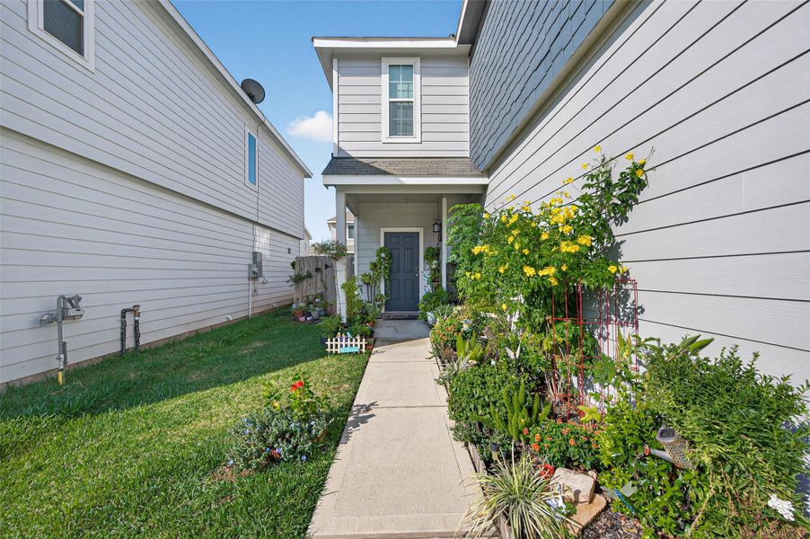 This welcoming home features a charming front walkway bordered by lush greenery and vibrant flowers. The modern exterior is accented by a neatly trimmed lawn, creating a cozy and inviting entrance.