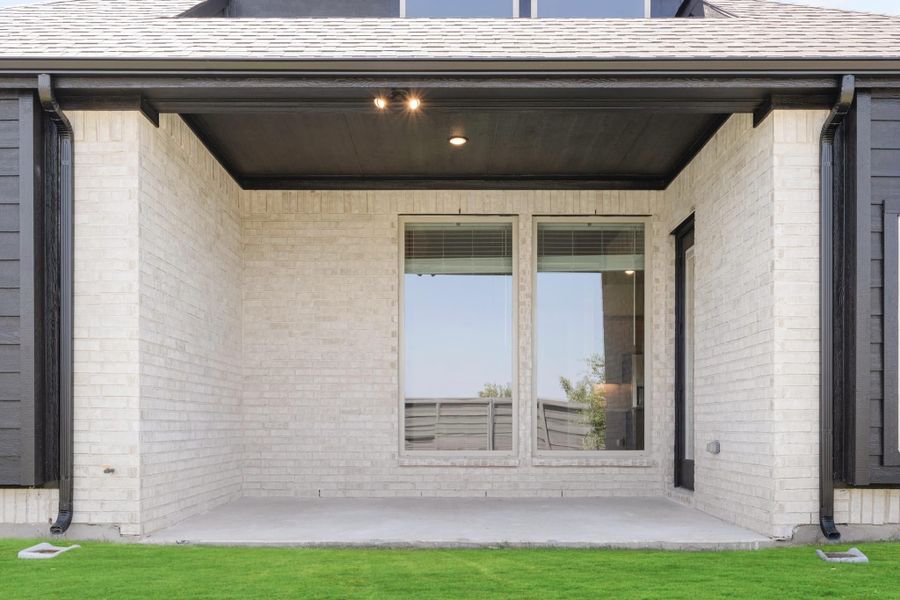 Covered back patio with light brick walls, recessed lighting, large windows, and concrete floor overlooking green lawn