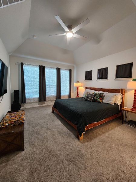 A comfortable bedroom features carpet flooring, vaulted ceilings, and a large window with ample natural light.
