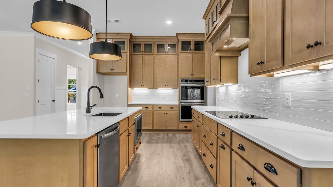 Kitchen with wood colored cabinetry and nearby gathering room (Representative of completed home)