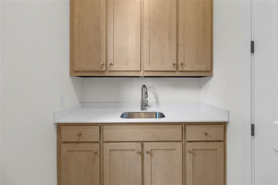 Utility area featuring light wood-finish cabinetry, a white countertop, and a stainless steel sink with a gooseneck faucet
