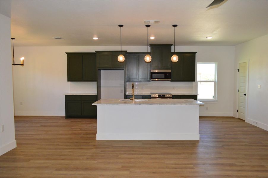 Kitchen with pendant lighting, a kitchen island with sink, appliances with stainless steel finishes, light stone countertops, and recessed lighting Kitchen with pendant lighting, a kitchen island with sink, appliances with stainless steel finishes, light stone countertops, and recessed lighting