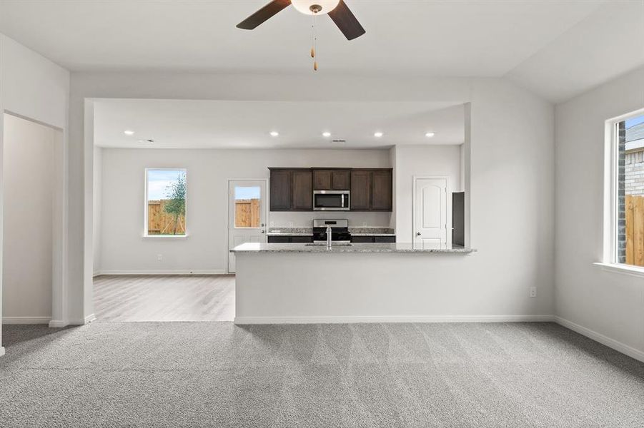 Kitchen featuring light colored carpet, dark brown cabinets, stainless steel appliances, light stone countertops, and recessed lighting Kitchen featuring light colored carpet, dark brown cabinets, stainless steel appliances, light stone countertops, and recessed lighting
