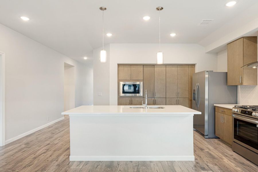 Modern kitchen with large white island, wood cabinets, stainless steel appliances, and pendant lights over hardwood floors