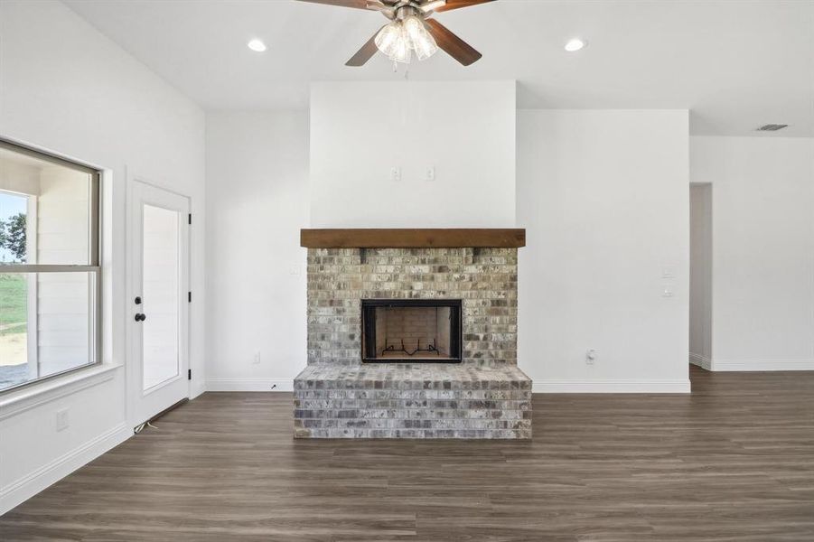 Unfurnished living room with ceiling fan, a brick fireplace, and dark wood-type flooring