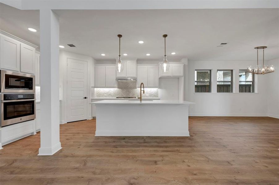 Kitchen featuring stainless steel appliances, white cabinetry, an island with sink, and light wood-type flooring