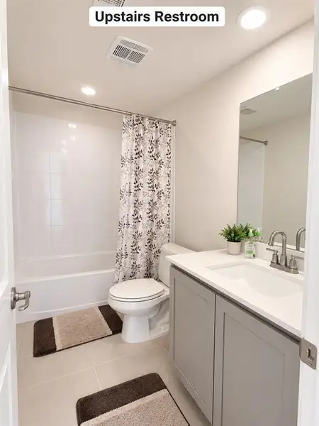 Bathroom featuring a built-in tub with white tile surround, a single vanity with a white countertop and undermount sink, a large mirror, and recessed lighting Bathroom featuring a built-in tub with white tile surround, a single vanity with a white countertop and undermount sink, a large mirror, and recessed lighting