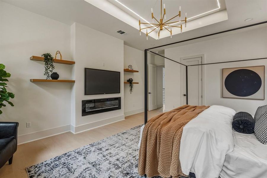 Bedroom featuring light wood finished floors, a chandelier, and a glass covered fireplace