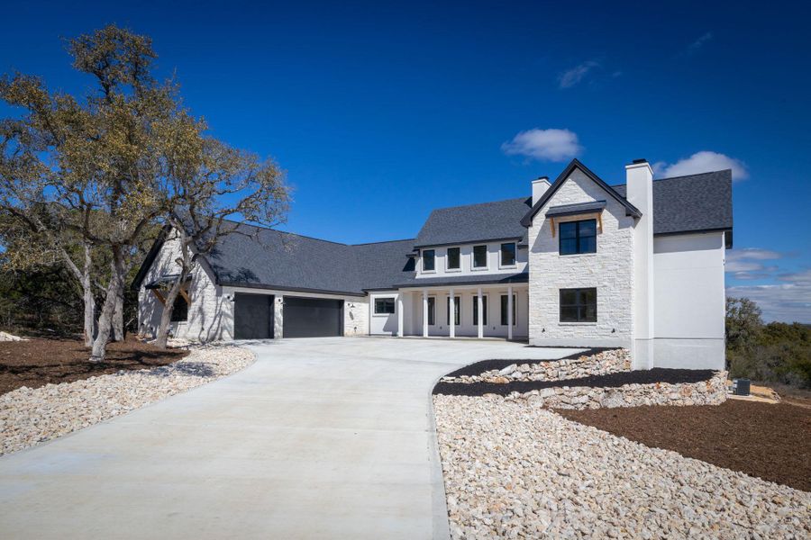 Modern farmhouse featuring stone siding, concrete driveway, a chimney, and an attached garage