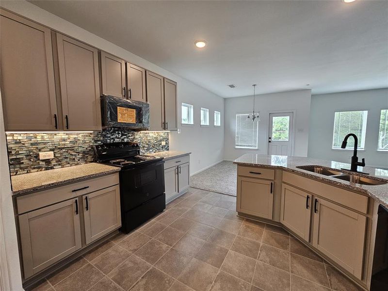 Kitchen featuring sink, tasteful backsplash, tile patterned floors, black appliances, and light stone counters