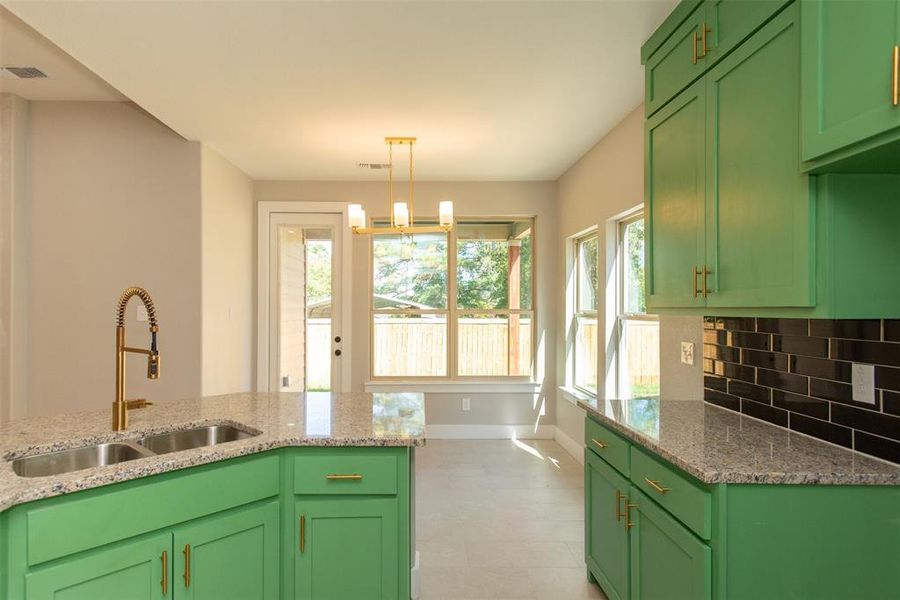 Kitchen featuring sink, decorative light fixtures, light stone counters, and green cabinets