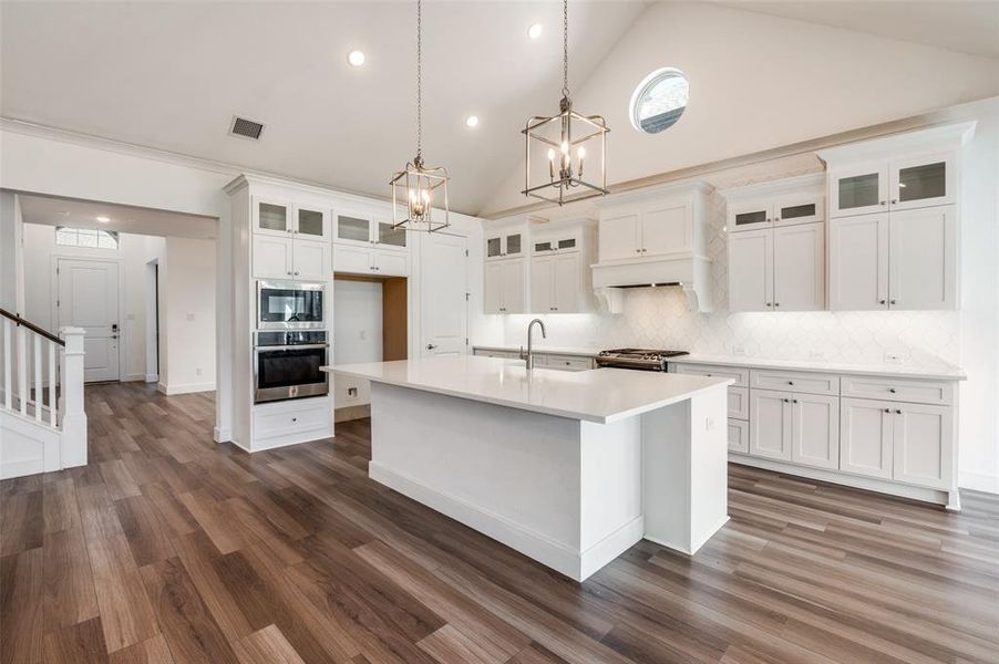 Kitchen featuring stainless steel appliances, glass insert cabinets, white cabinetry, high vaulted ceiling, and tasteful backsplash Kitchen featuring stainless steel appliances, glass insert cabinets, white cabinetry, high vaulted ceiling, and tasteful backsplash