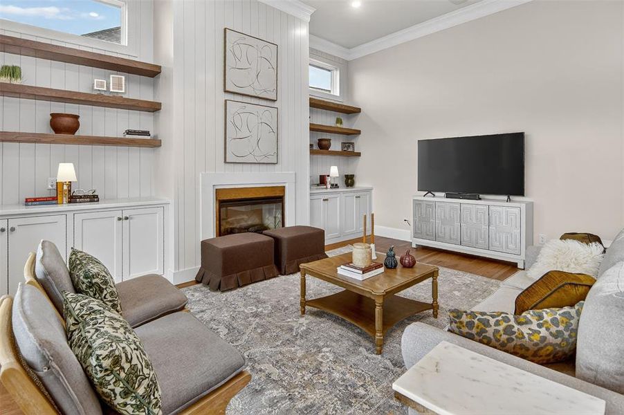 Living area with a glass covered fireplace, ornamental molding, wood finished floors, and built in shelves