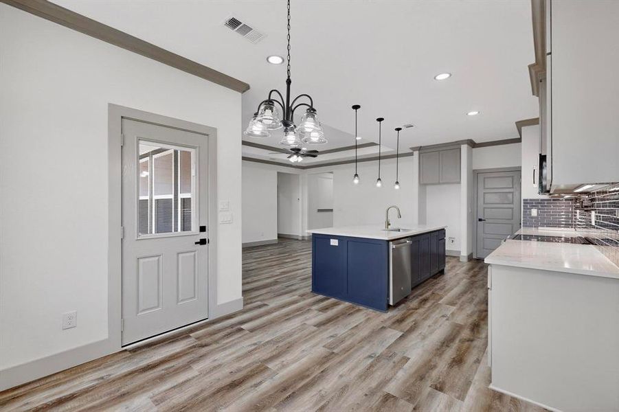 Kitchen featuring a chandelier, decorative light fixtures, light stone countertops, crown molding, and an island with sink