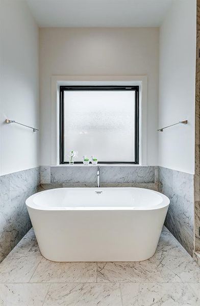 This modern primary bathroom showcases a freestanding bathtub, surrounded by elegant marble tile. A large frosted window provides natural light while maintaining privacy.