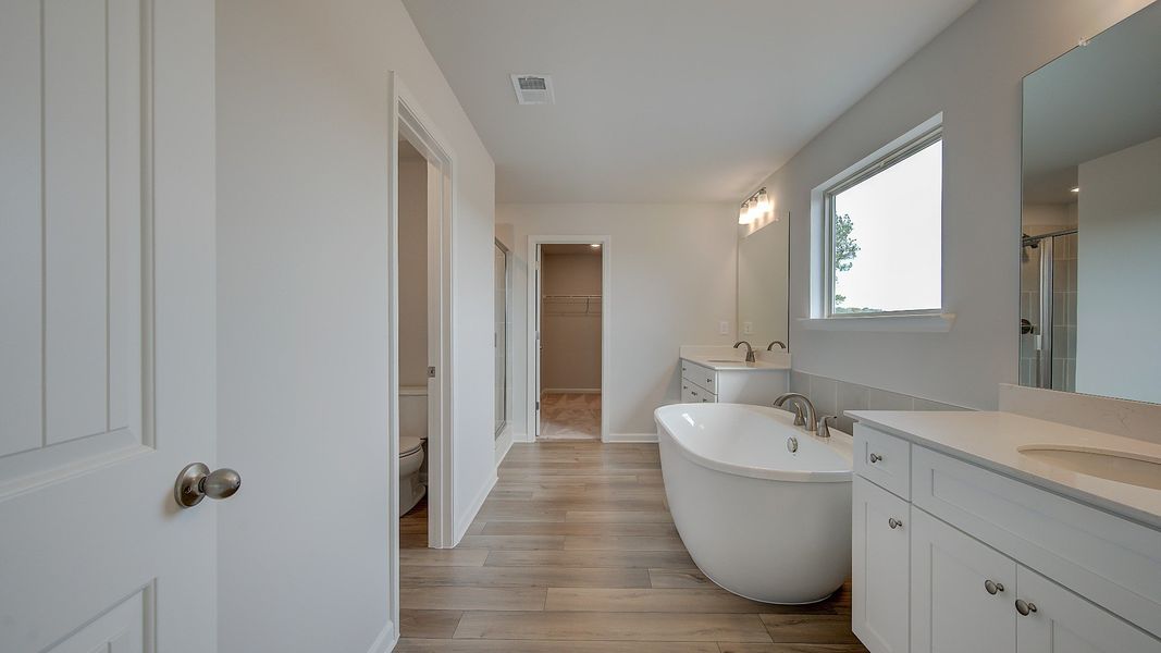 Primary bath with modern tile flooring, freestanding tub, and dual vanities in the Stonefield at Brighton.