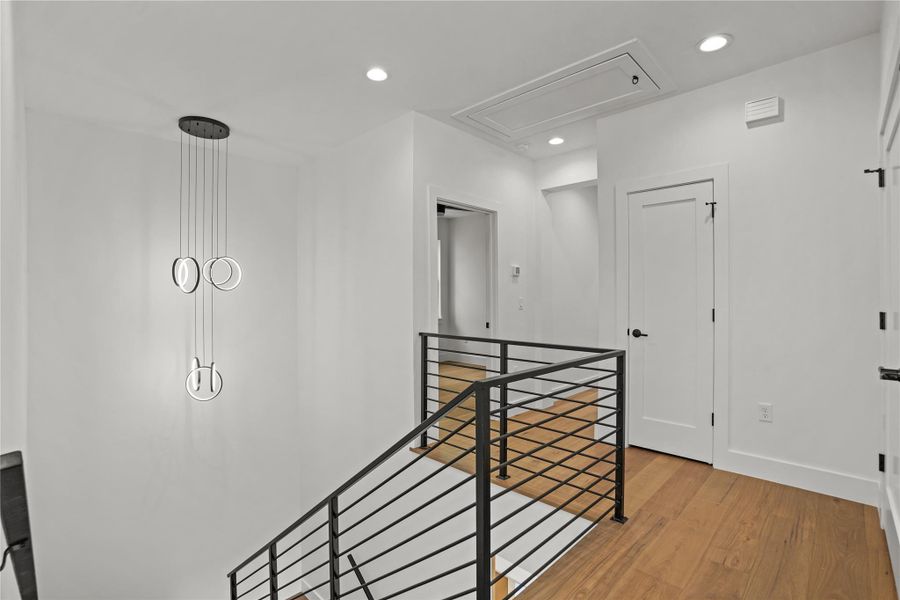 Clean lines define this bright stairwell, featuring sleek wood flooring and a modern chandelier.
