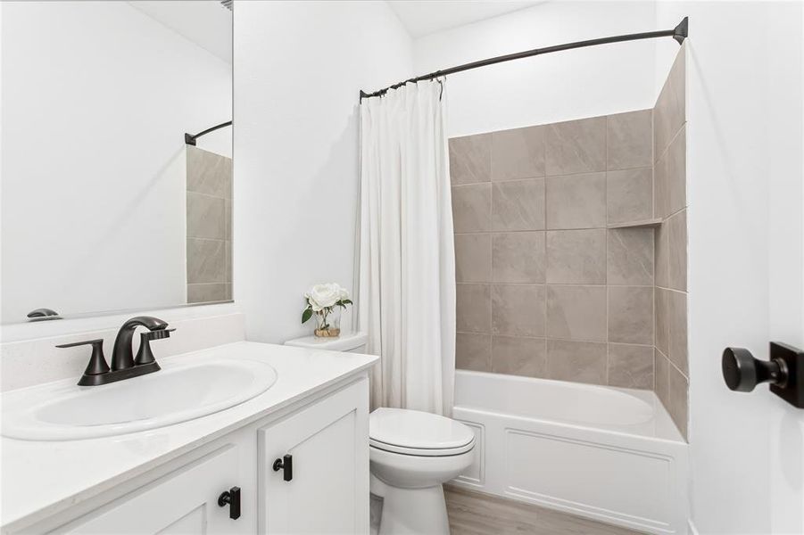 Bathroom featuring a white vanity with a dark faucet, a toilet, and a bathtub with light gray tiled walls