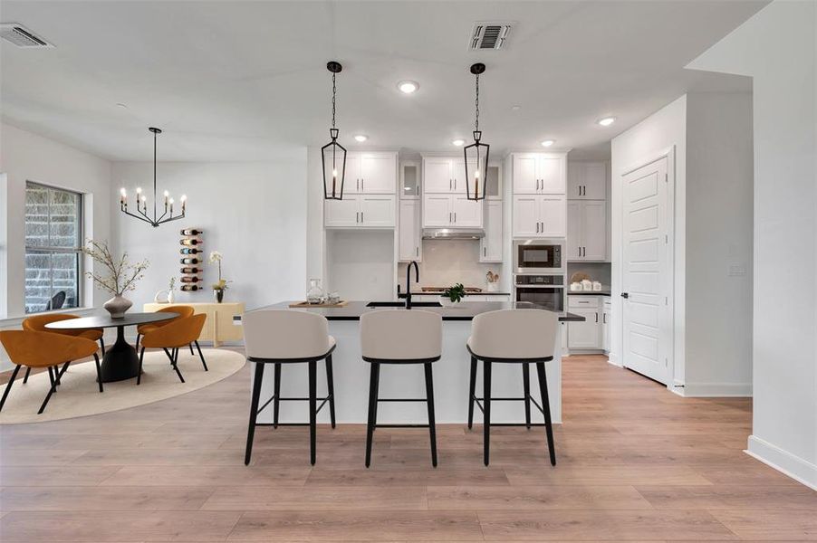 Contemporary kitchen featuring a large island with seating, white cabinetry, dark countertops, and stainless steel appliances Contemporary kitchen featuring a large island with seating, white cabinetry, dark countertops, and stainless steel appliances