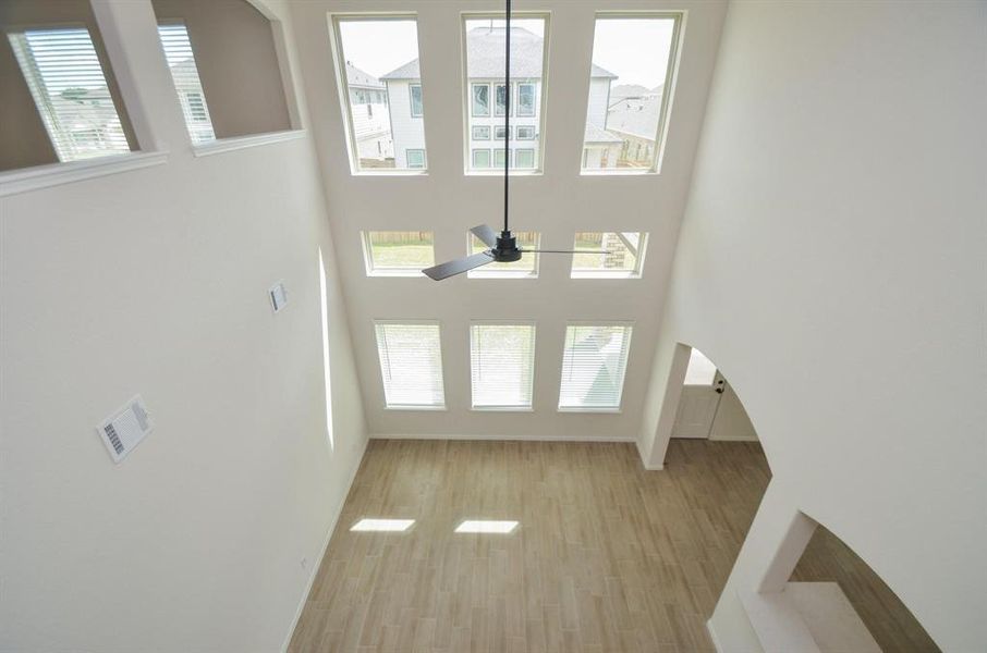 A breathtaking two-story living room flooded with natural light, thanks to expansive windows that stretch from floor to ceiling. The space offers a modern ceiling fan, open layout, and sleek wood-like tile floors. Perfect for entertaining, this grand room creates a dramatic yet inviting atmosphere.