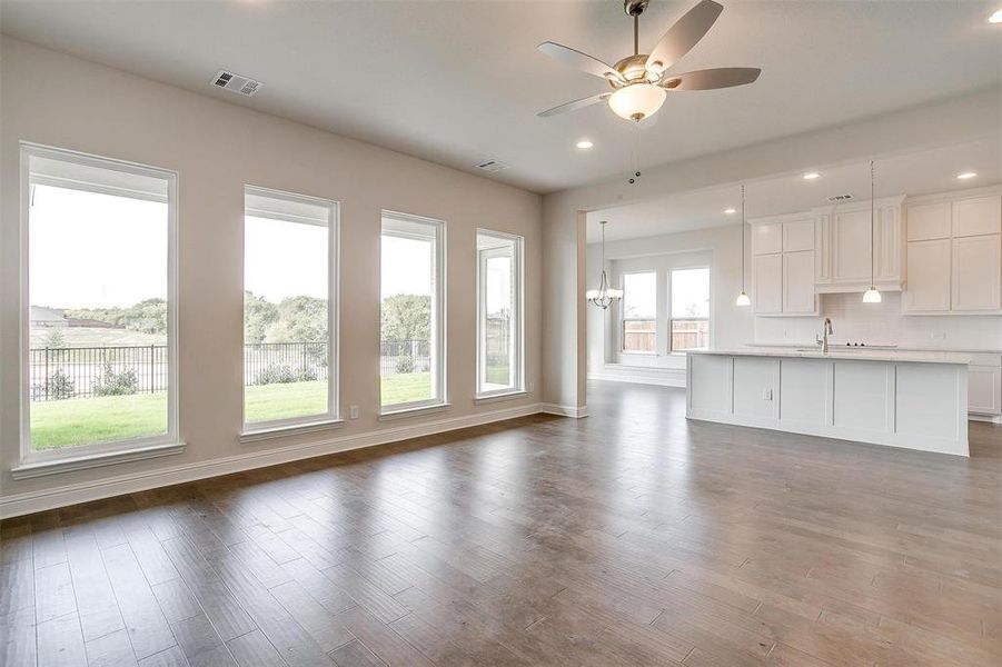 Unfurnished living room with sink, ceiling fan with notable chandelier, plenty of natural light, and dark hardwood / wood-style flooring