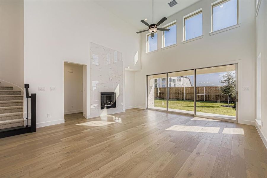 Unfurnished living room with stairway, light wood-style flooring, a fireplace, a high ceiling, and a ceiling fan