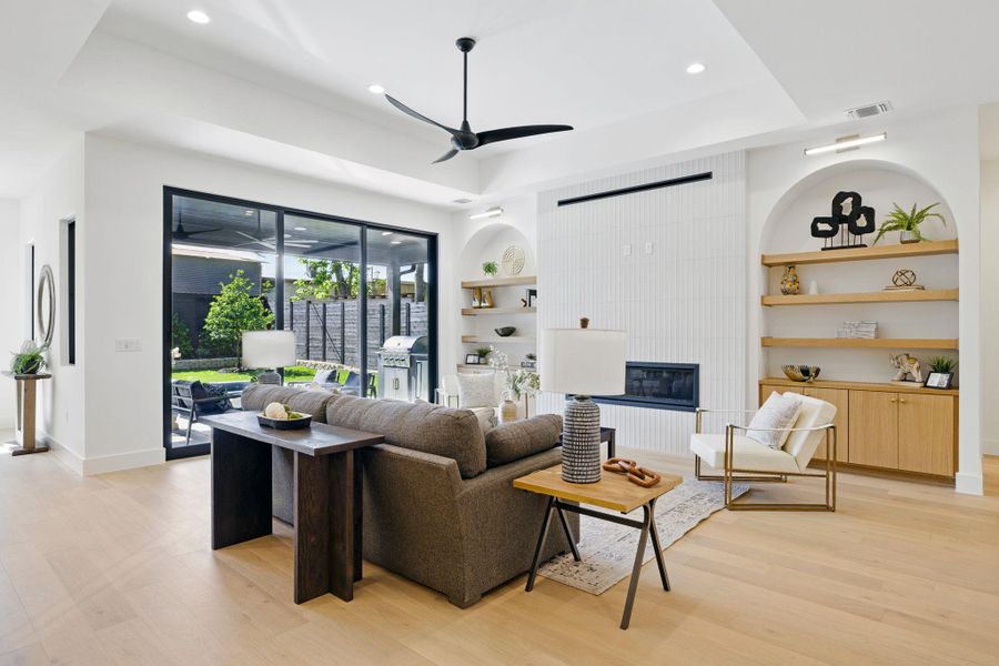 Living room featuring built in shelves, a ceiling fan, light wood-style floors, a fireplace, and recessed lighting