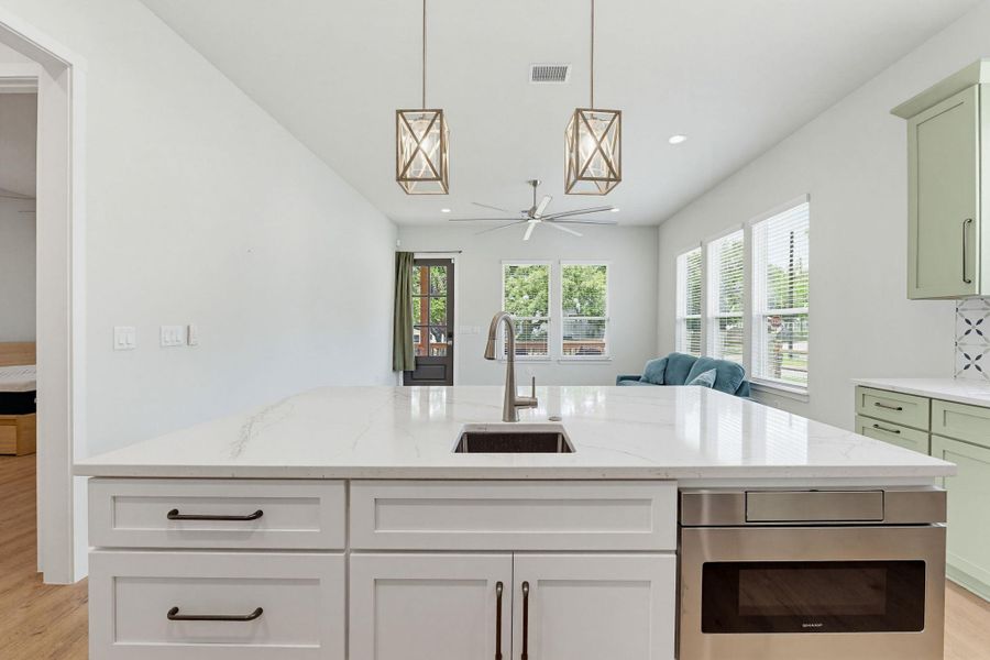 A bright open concept kitchen with a spacious island, integrated sink, and contemporary lighting fixtures.