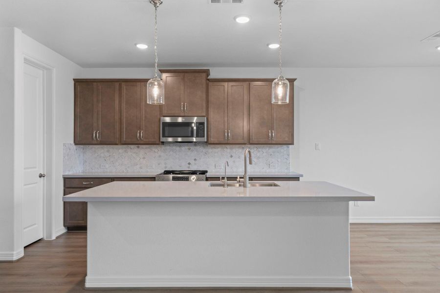 This light and bright kitchen features a large quartz island, white cabinets, a large sink overlooking your family room, recessed lighting, and beautiful backsplash.