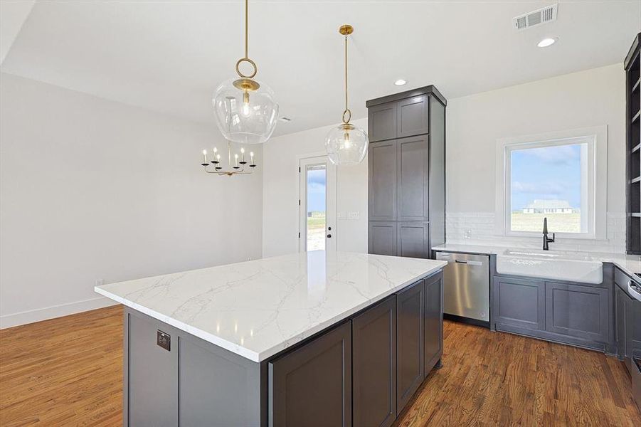 Kitchen with light stone counters, dishwasher, dark wood-type flooring, pendant lighting, and a center island