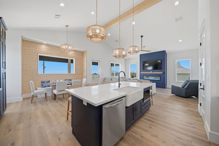 This spacious open-concept living area features a modern kitchen with a large island and farmhouse sink, elegant pendant lighting, and stylish wood accents. The adjacent dining area is bright and inviting, while the cozy living space includes a built-in fireplace and large windows, offering plenty of natural light.