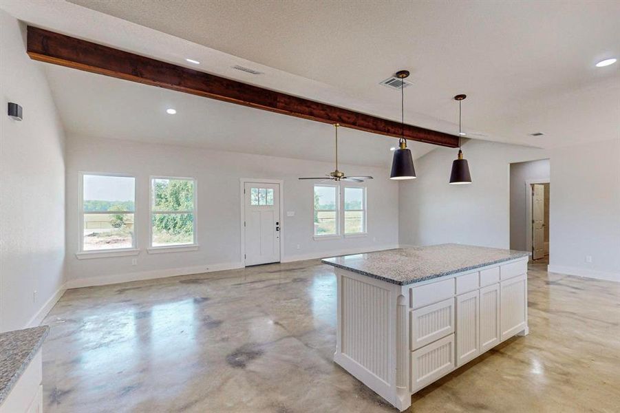 Kitchen with pendant lighting, white cabinetry, vaulted ceiling with beams, light stone countertops, and a kitchen island