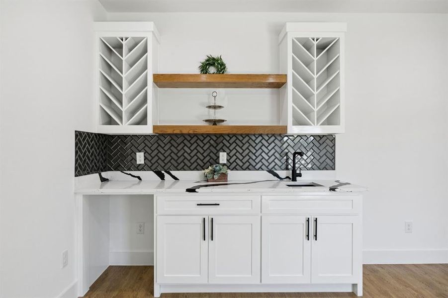 Bar featuring tasteful backsplash, white cabinets, light stone counters, and open shelves