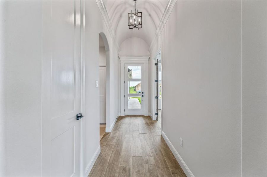 Corridor featuring arched walkways, light wood finished floors, baseboards, a chandelier, and vaulted ceiling