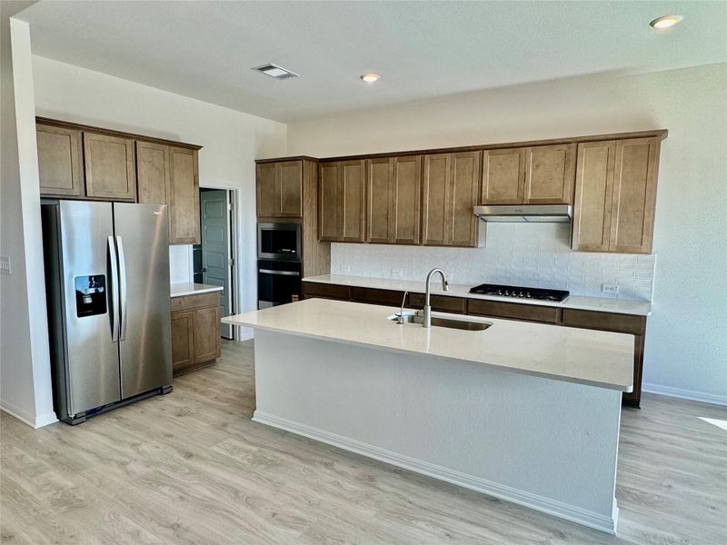Kitchen featuring stainless steel appliances, light wood finished floors, decorative backsplash, a center island with sink, and recessed lighting