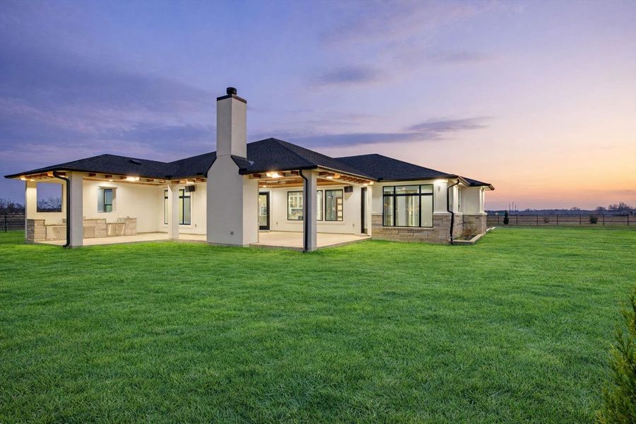 Back of house at dusk featuring a fenced backyard, a patio, a chimney, and stucco siding