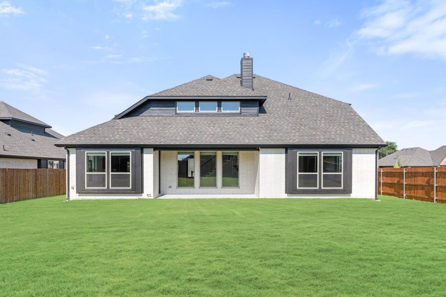 Rear exterior of single-story brick home with large windows, chimney, and fenced backyard with green lawn Rear exterior of single-story brick home with large windows, chimney, and fenced backyard with green lawn