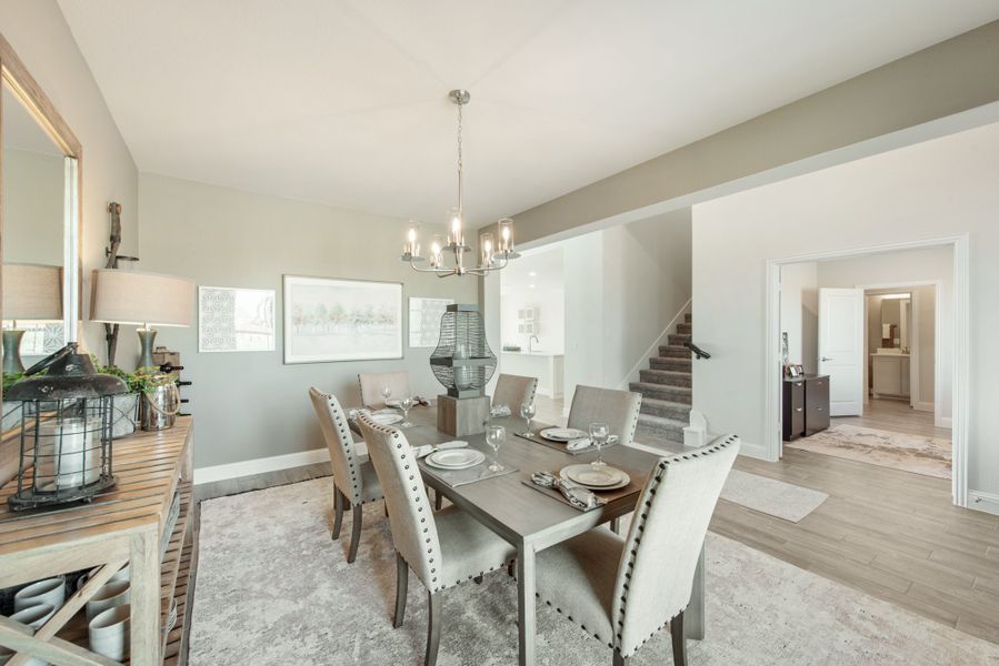 Dining room with gray table, six upholstered chairs, chandelier, and staircase visible in background