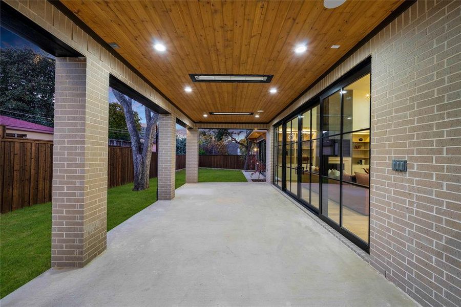 Covered patio featuring a wood-finish ceiling with recessed lighting, exposed brick pillars, and a concrete slab floor