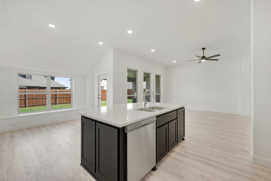 Kitchen island with dark cabinets, white countertop, and stainless steel sink open to living area with light wood floors