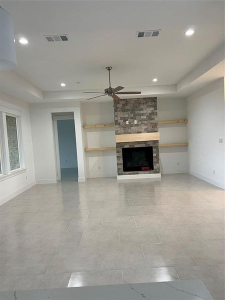 Unfurnished living room with a raised ceiling, ceiling fan, and a stone fireplace