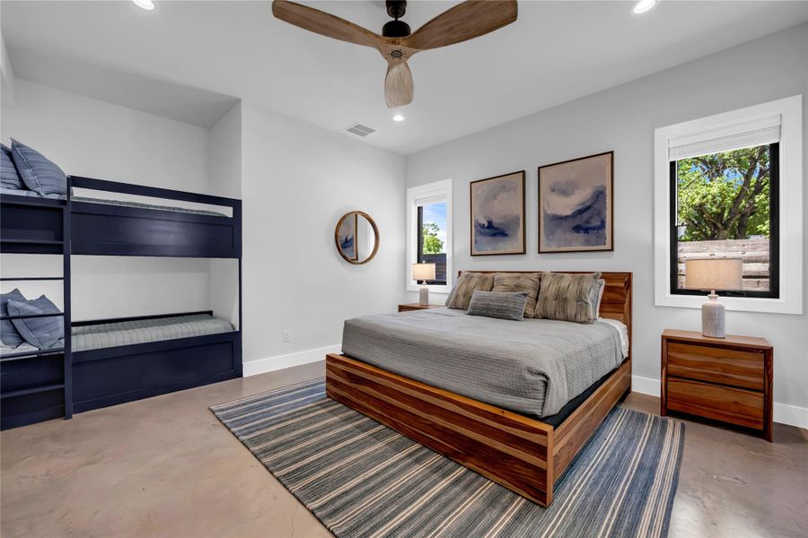 Bedroom three: Concrete flooring with a striped area rug, a wood-finish bed frame, and built-in bunk beds with a navy finish