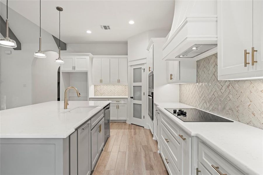 Kitchen with a center island with sink, decorative light fixtures, white cabinetry, light stone countertops, and recessed lighting