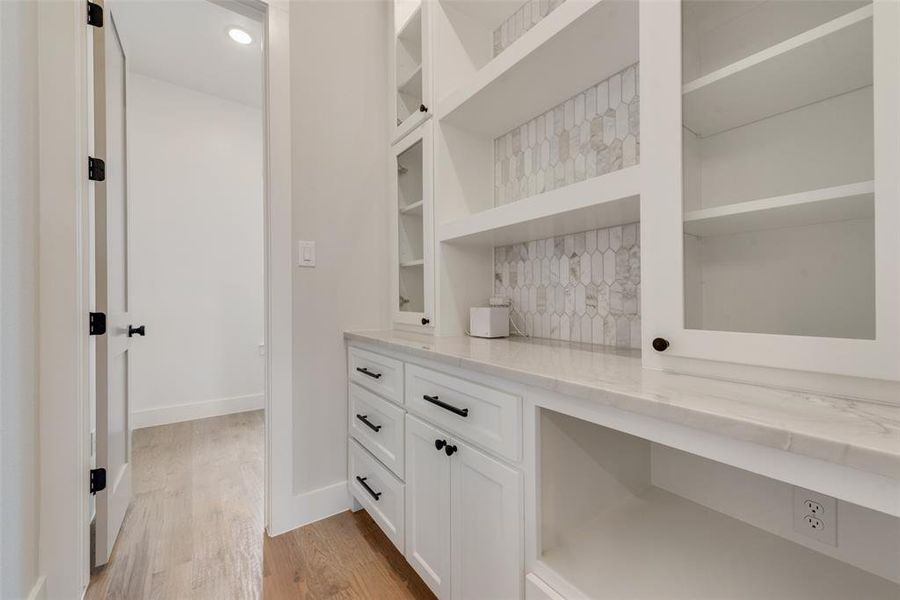 Bar with white cabinetry, light stone counters, and light hardwood / wood-style flooring