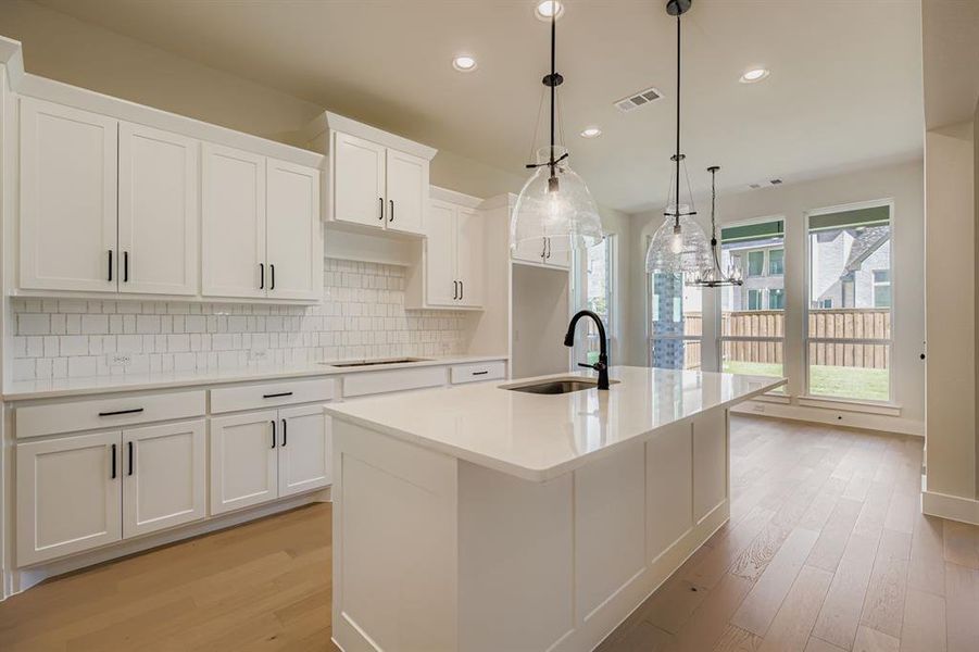 Kitchen featuring white cabinetry, decorative backsplash, an island with sink, recessed lighting, and light stone counters