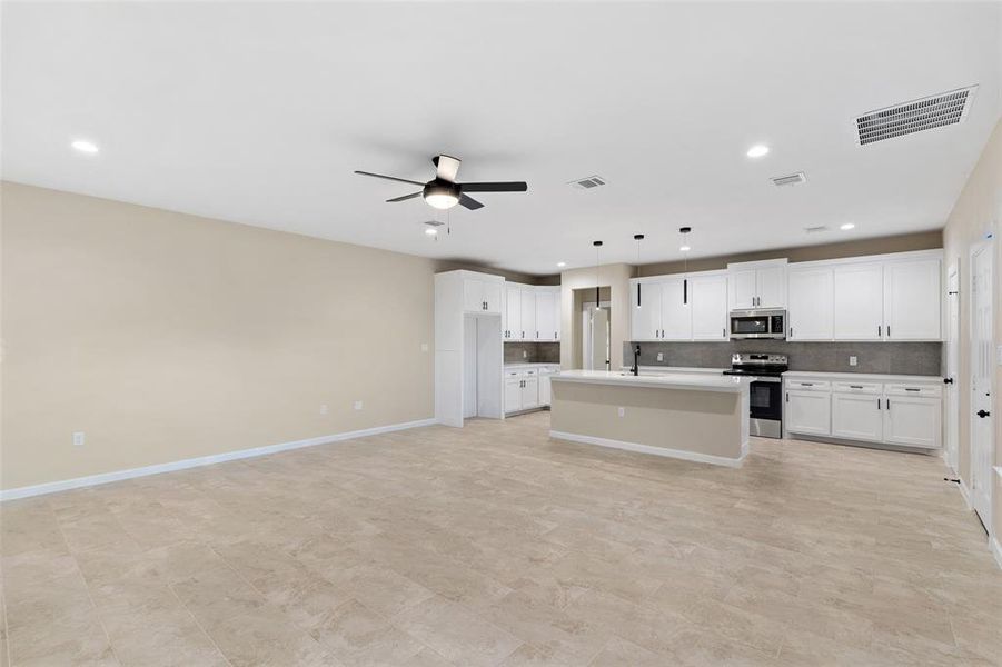 Kitchen featuring white cabinetry, a kitchen island with sink, hanging light fixtures, decorative backsplash, and appliances with stainless steel finishes