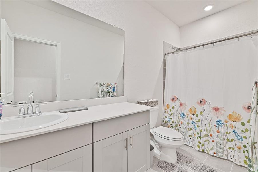 Bathroom featuring curtained shower, toilet, vanity, and tile patterned flooring