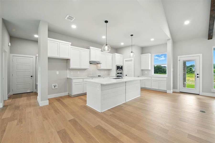 Kitchen with a kitchen island with sink, white cabinets, light countertops, decorative backsplash, and recessed lighting Kitchen with a kitchen island with sink, white cabinets, light countertops, decorative backsplash, and recessed lighting